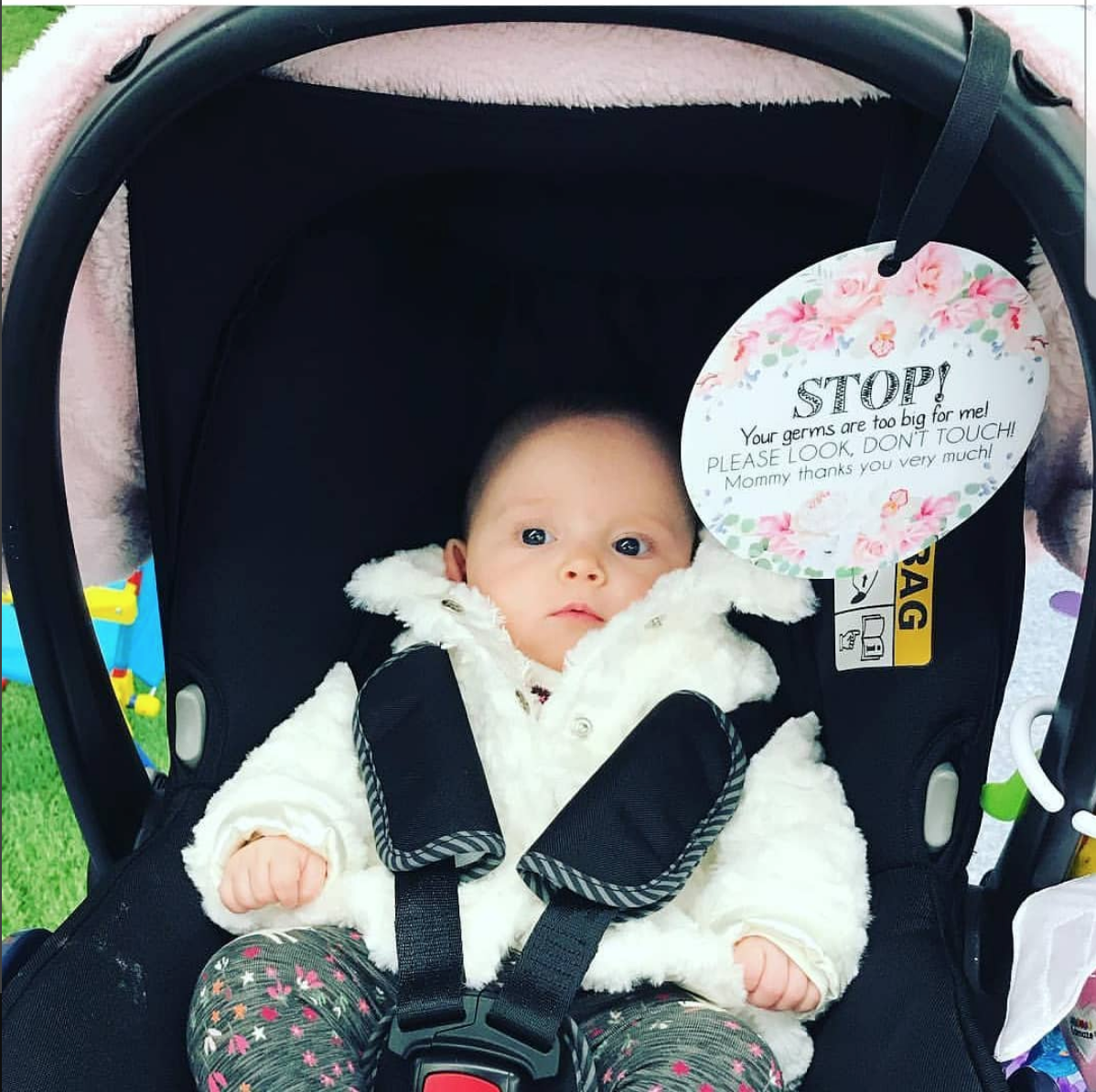 Little newborn girl in her car seat with a stop no touching baby sign preemie gift